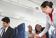 A flight attendant serving drinks to two passengers on an airplane, illustrating the experience of drinking alcohol on an airplane.