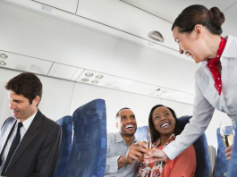 A flight attendant serving drinks to two passengers on an airplane, illustrating the experience of drinking alcohol on an airplane.