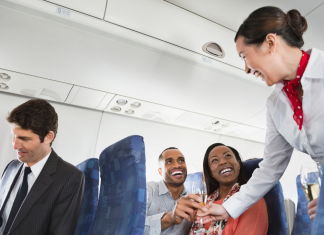 A flight attendant serving drinks to two passengers on an airplane, illustrating the experience of drinking alcohol on an airplane.