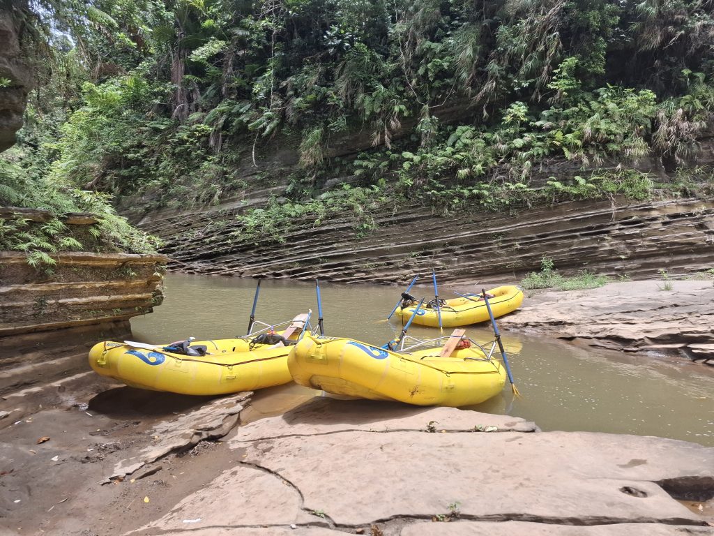 Bright yellow rafts resting on the rocky shores of the Upper Navua River, surrounded by lush green foliage and layered volcanic rock formations in Fiji