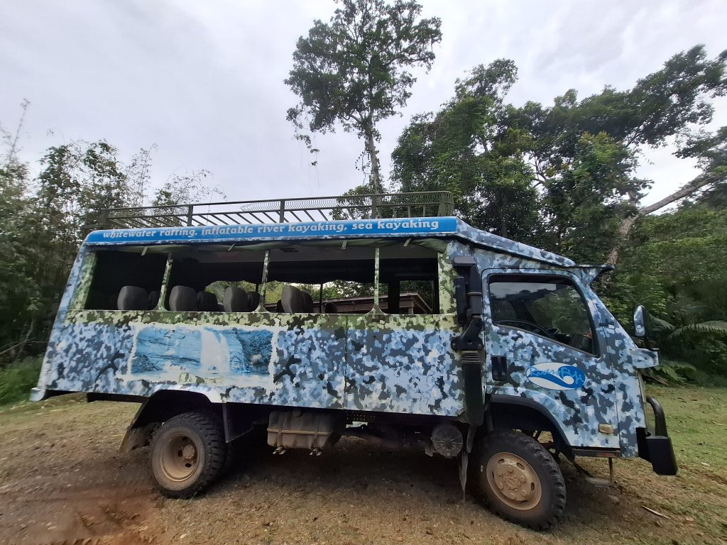 Rivers Fiji transport vehicle used for whitewater rafting and kayaking adventures, parked amidst lush greenery in Fiji.