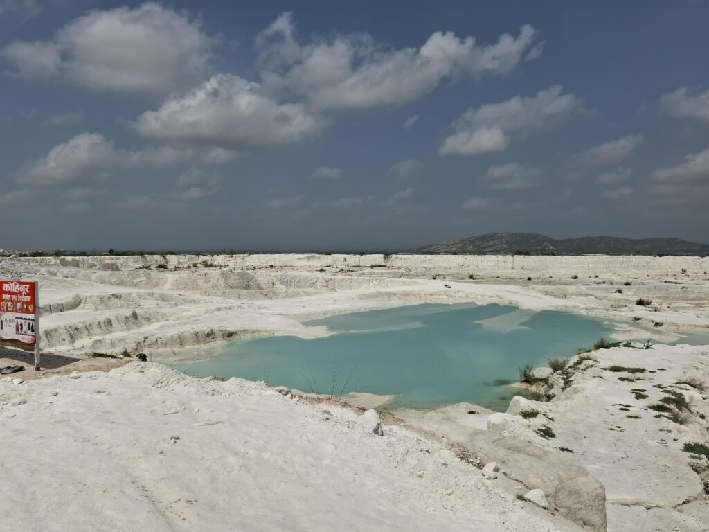 Turquoise pool in a white hollow, with a red sign at the edge, Kishangarh dumping yard
