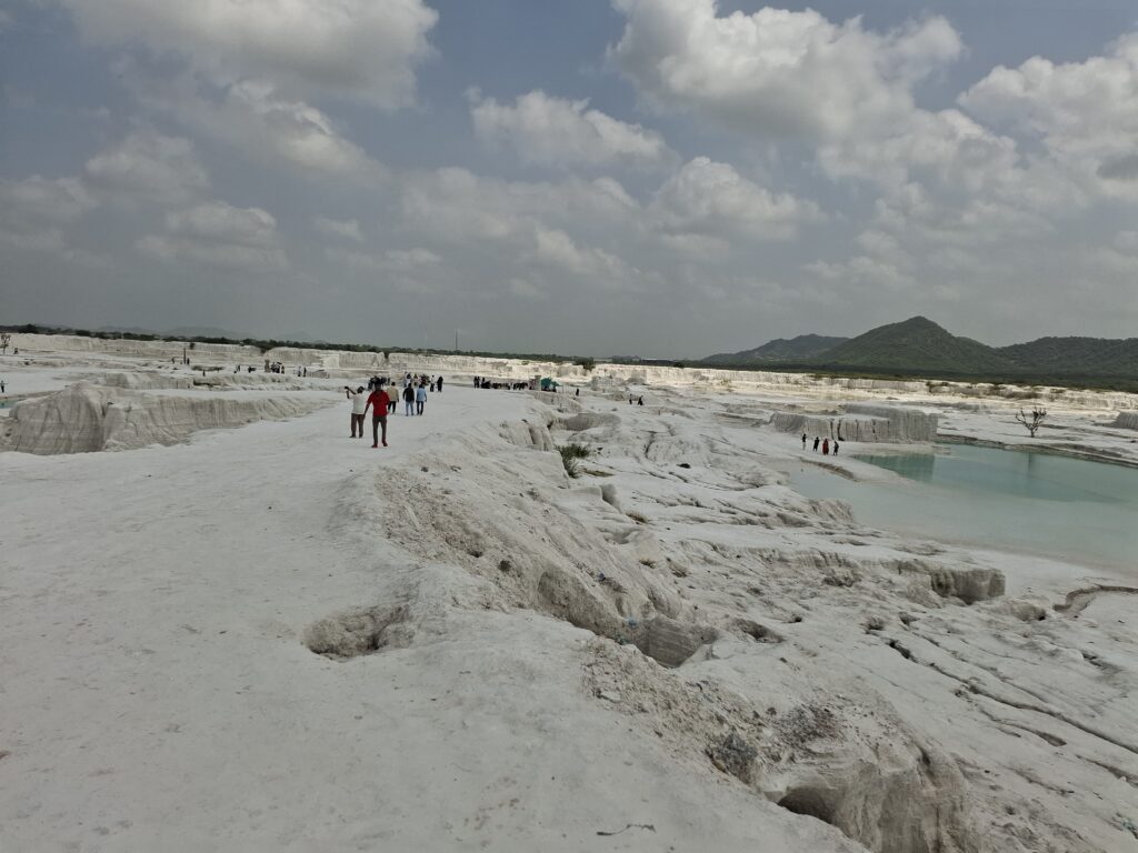 Visitors walking along a white ridge above a turquoise pool at Kishangarh dumping yard